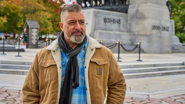 A man in a brown coat standing in front of the Natio<em></em>nal War Memorial in Ottawa.