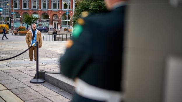 A man in a brown jacket looks at the Natio<em></em>nal War Memorial, wher<em></em>e the shoulder of a soldier standing sentry is visible in the foreground, out of focus.