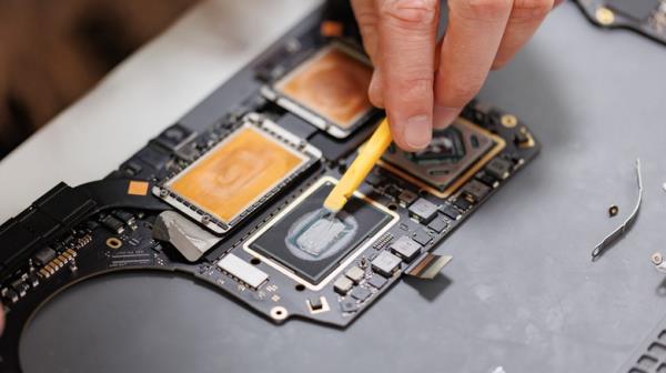 A hand applying thermal paste to a MacBook.